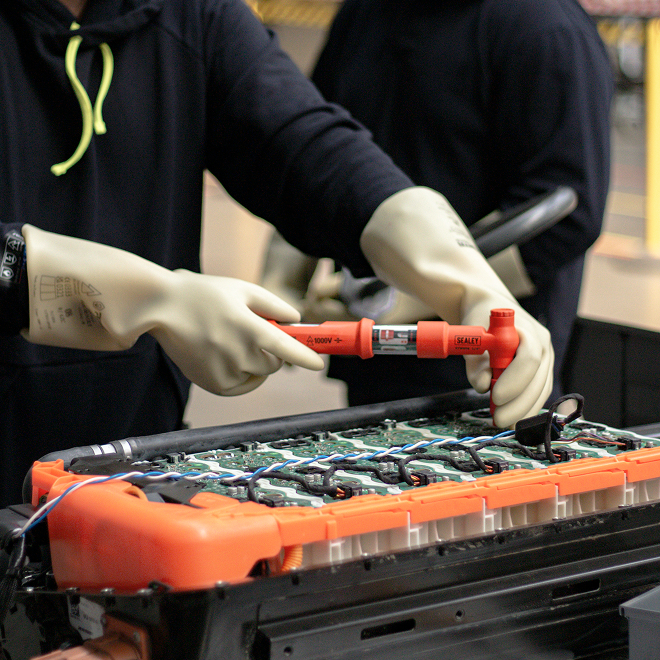 a person wearing gloves carrying out EV battery checks